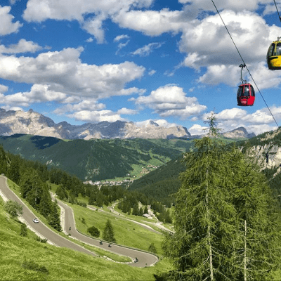 Yellow and red chairlifts on Gardena Pass in Dolomites Italy, green valley and winding road